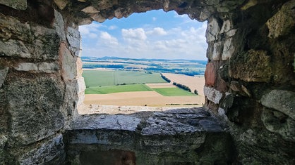 Die Aussicht aus der Steinmauer der Burgruine auf Felder und Hügel in der Ferne.