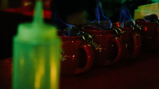 Mehrere rote Tassen mit Feuerzangenbowle stehen nebeneinander auf einer Theke.