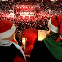 Tausende Menschen stehen mit Liedertexten und Kerzen in den Händen und Weihnachtsmützen auf dem Kopf in einem Stadion