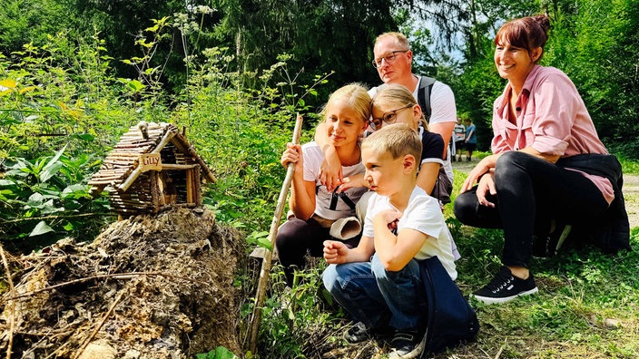 Eine Familie, bestehend aus drei Kindern und zwei Erwachsenen, schaut sich zufrieden eines der Wichtelhäuser im Wichtelwald an.