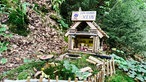 Ein aus Holz gebasteltes Miniatur-Häuschen steht im Wald und stellt einen Wichtel-Biergarten dar.