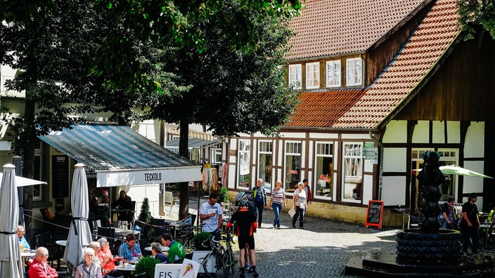 Eine Szenerie aus der historischen Altstadt Tecklenburgs mit einem Café links, Fachwerkhaus in der Mitte und Brunnen rechts.