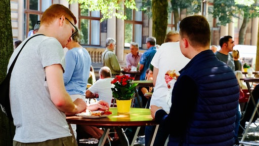Zwei junge Männer von hinten an einem Stehtisch und essen auf dem Wochenmarkt in Münster.