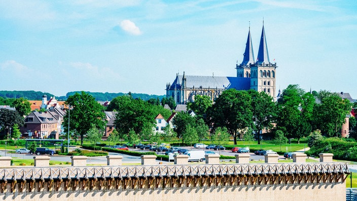 Blick auf Xanten mit Grün im Vordergrund und Kirche und Häusern im Hintergrund.