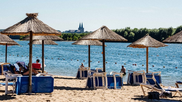 Strand des Naturbads Xantener Südsee. Besucher sitzen unter Strohschirmen.