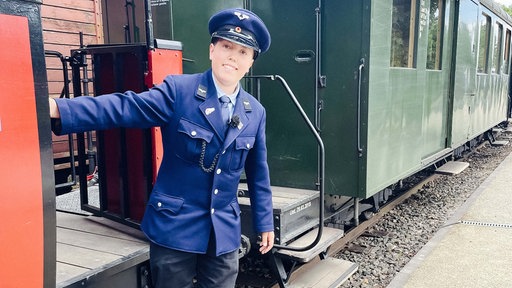 Leo steht stolz, gekleidet in seine Uniform, an einem historischen Eisenbahnwagon.
