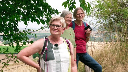 Landschaftsführerin Maria Theresia Herbold im Interview. Im Hintergrund stehen zwei Frauen.