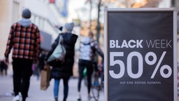 Auf einem Aufsteller vor einem Geschäft in einer Fußgängerzone steht "Black Week 50%" 