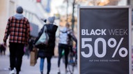Auf einem Aufsteller vor einem Geschäft in einer Fußgängerzone steht "Black Week 50%" 