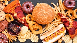 Das Beitragsbild des Dok 5 "Fastfood - Gute Geschäfte mit schnellem Essen" zeigt einen Mix aus Fastfood verteilt auf dunklem Hintergrund. Pizza, Hamburger, Frittten, Chips, Hot Dog, Süßigkeiten 