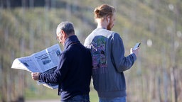 Symbolbild Boomer vs. Millennial: Ein älterer Mann liest Zeitung, ein jüngerer schaut auf sein Smartphone