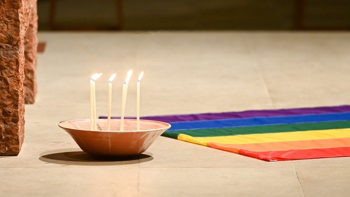Das Beitragsbild des WDR3 Kulturfeature "Herz über Kreuz" zeigt den Altar der Paulskirche, Kerzen und eine Regenbogenfahne.