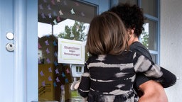 Schild an der Eingangstür einer Betreuungseinrichtung: "Kita geschlossen wegen Personalmangel", Kind auf dem Arm eines Erwachsenen.