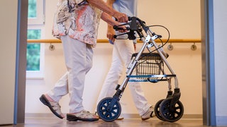 Pflegekraft geht in einem Pflegeheim mit einer Bewohnerin über einen Korridor