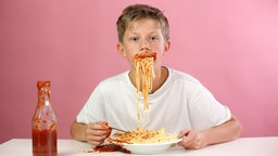 Junge isst Spaghetti mit Ketchup, der rund um seinen Mund verschmiert ist