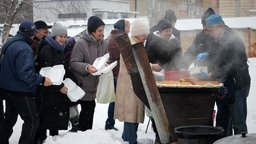 Menschen stehen bei Kälte an einer Essensausgabe unter freiem Himmel an, wo sie von Freiwilligen mit einer warmen Mahlzeit versorgt werden. (07.02.2026)