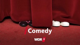 Zwei Paar Schuhe lugen unter einem roten Vorhang hervor. 