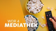 Hand an einer Fernbedienung neben zwei Schalen Popcorn