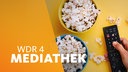 Hand an einer Fernbedienung neben zwei Schalen Popcorn