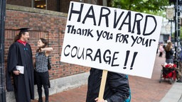 Das Beitragsbild des Dok5 Feature "Wissenschaft unter Druck" zeigt einen Unterstützer der Harvard University im Kampf gegen Trumps Regierung die Zuschüsse kürzt.   
