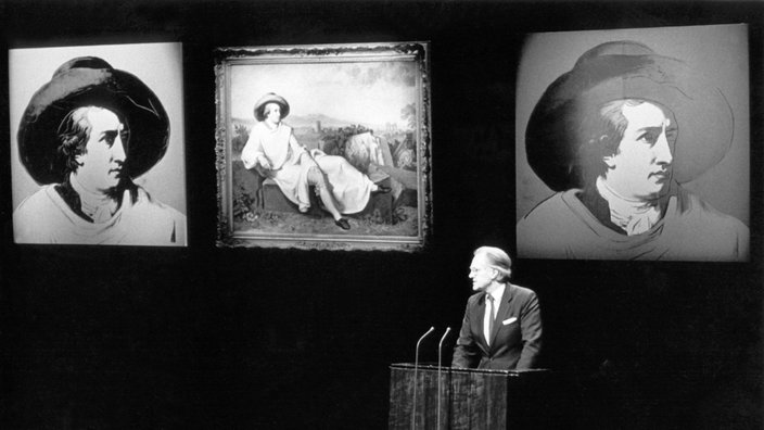 Hilmar Hoffmann hält am 21. März 1982 zu Beginn einer Goethe-Matinee zum Wettbewerb "Mein Goethe" im Schauspielhaus die Begrüßungsrede. Im Hintergrund das Tischbein-Gemälde "Goethe in der Campagna" sowie zwei Warhol-Verfremdungen. 