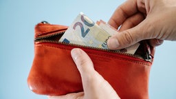 Eine Person nimmt Scheine aus einer roten Geldbörse.