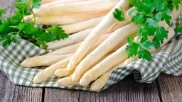 Frischer weißer Spargel mit Persilie in einem Korb auf einem Holztisch.