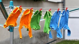 Orangene, grüne und blaue Babystrampler trocknen auf einer Wäscheleine