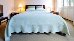 Ein Doppelbett in einem Schlafzimmer mit einem hellblauen Bettüberwurf