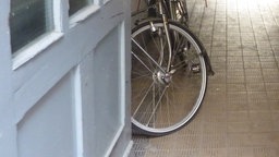 Eine weiße, offene Tür mit einem schwarzen Schmutzstreifen, hinter der ein Fahrrad steht, von dem man im Bildausschnitt nur den Reifen sieht.