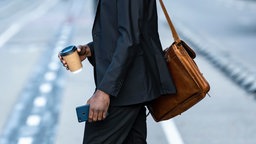 Ein Mann im schwarzen Anzug mit einer Ledertasche überquert die Straße
