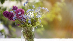 Eine große Glasvase mit verschiedenen Blumen auf einem Tisch im Freien. 