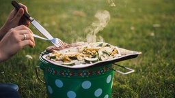 Eine Frau dreht Würstchen auf einem Grill auf einer Wiese. 