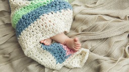 Die Füße eines Babys schauen aus einer Häkeldecke, in die das Baby eingewickelt ist
