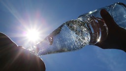 Eine Frau trinkt im Sonnenschein aus einer Flasche sprudelndes Mineralwasser. 
