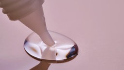 Aus einer Kleberflasche tropft Kleber auf einen rosanen Untergrund