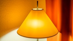 Ein gelber Lampenschirm auf einer eingeschalteten Lampe, von der Lampe geht warmes Licht aus.