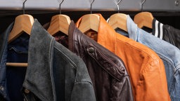 Verschiedene Jacken, darunter verschiedene Lederjacken, an Kleiderbügeln an einem Kleiderständer. 