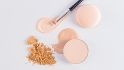 Make-up und Puder liegen verstreut und verschüttet auf weißem Untergrund 