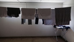 Ein Keller, in dem eine Wäscheleine aufgespannt ist, an der Kleidung hängt. 