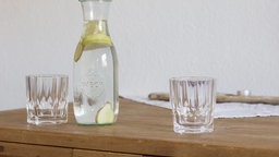Glaskaraffe mit zwei Gläsern auf einem Naturholztisch. 