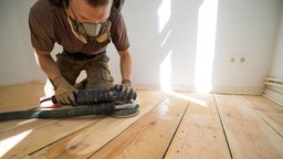 Ein Handwerker schleift eine Dielenboden mit einem Handschleifgerät.
