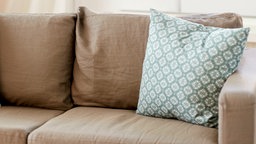 Ein Sofa mit hellbraunem Polster. Auf dem Sofa befindet sich ein dekoratives Kissen.