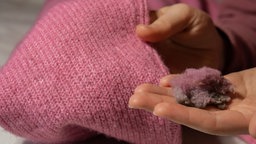 Eine Frau hält in der einen Hand einen pinken Pullover und in der anderen Hand eine Ansammlung an Fusseln