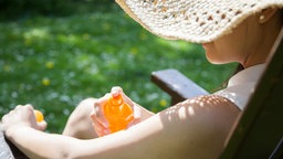 Eine junge Frau sitzt in einem Park und trägt Sonnencreme auf