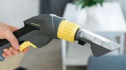 Eine Männerhand hält den Sprüh- und Saugaufsatz eines Sprühextraktionsgeräts.