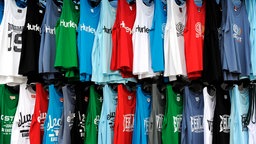 In zwei Reihen hängen bunte T-Shirts und Tops mit verschiedenen Aufdrucken