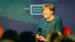 Angela Merkel mit Mikrofon auf der Bühne beim WDR Europaforum 2026 in Berlin