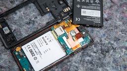 Ein Smartphone liegt geöffnet auf einem Tisch, der herausgenommene Akku liegt daneben