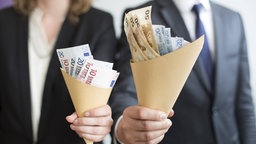 Mann und Frau halten jeweils ein Bündel Geld in die Kamera.